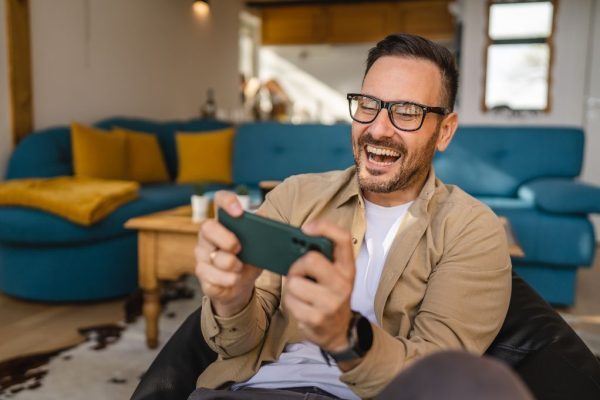 An adult male sitting on his couch, while enjoying a casino game on his smartphone.