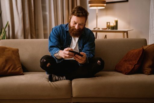 Red haired man with beard excitedly playing mobile game on couch